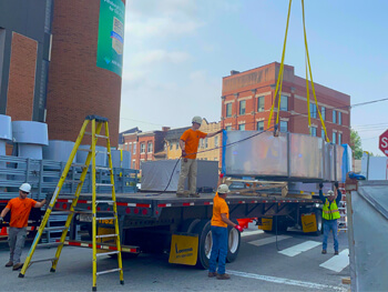 Workers hoisting HVAC equipment from back of a truck with a crane